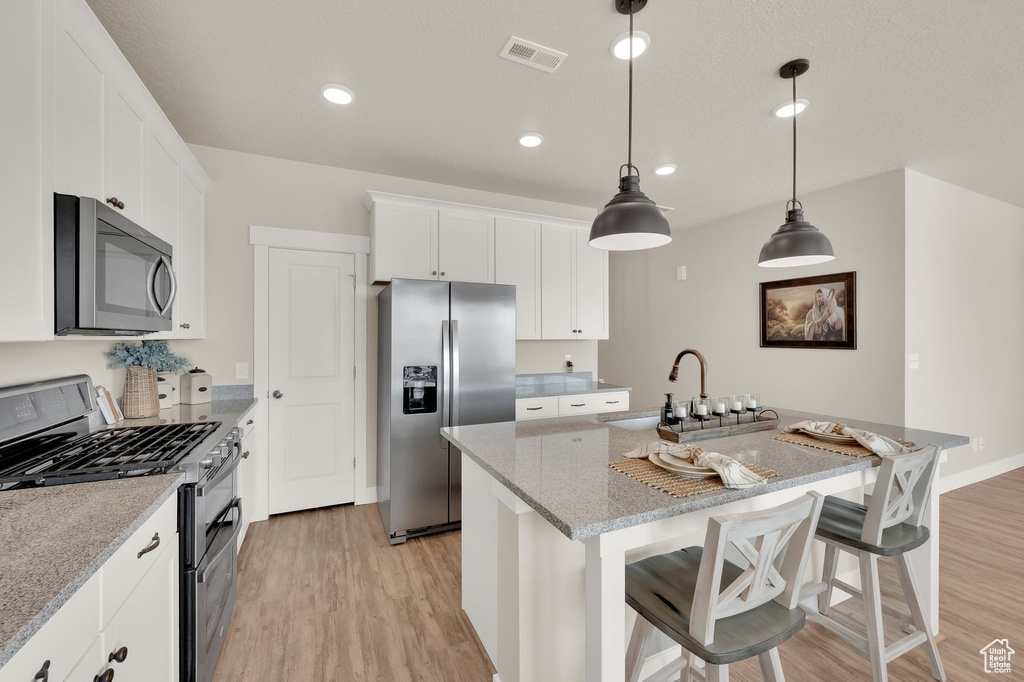 Kitchen with appliances with stainless steel finishes, light wood-type flooring, a sink, a kitchen island with sink, and white cabinets
