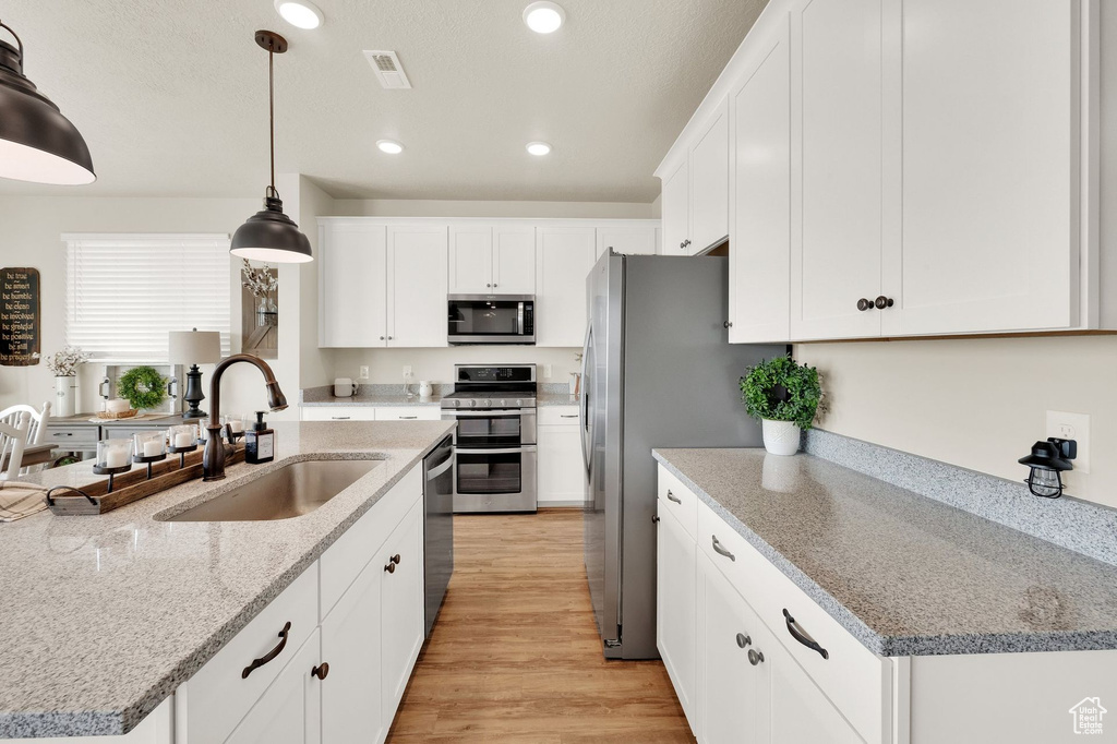 Kitchen featuring appliances with stainless steel finishes, a sink, recessed lighting, white cabinets, and light wood-style floors