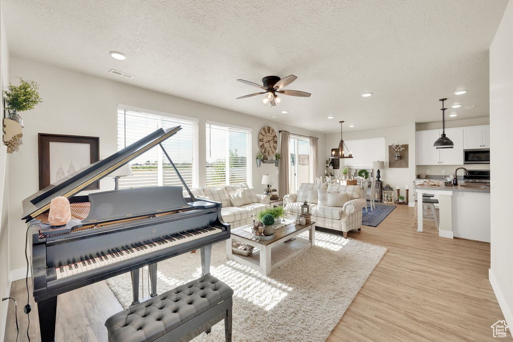 Living room featuring a ceiling fan, light wood-style floors, a textured ceiling, recessed lighting, and baseboards