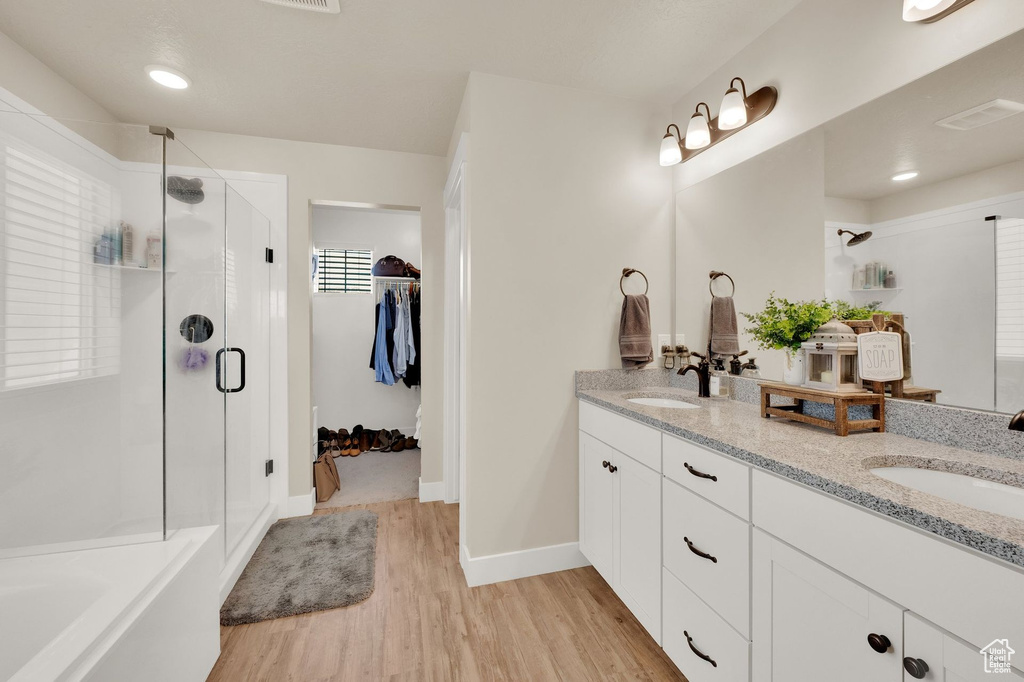 Bathroom featuring a stall shower, double vanity, wood finished floors, a spacious closet, and a bath