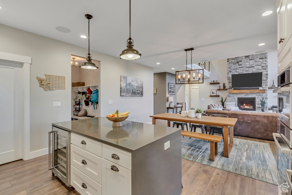 Kitchen with beverage cooler, a fireplace, light wood-style flooring, white cabinetry, and dark countertops