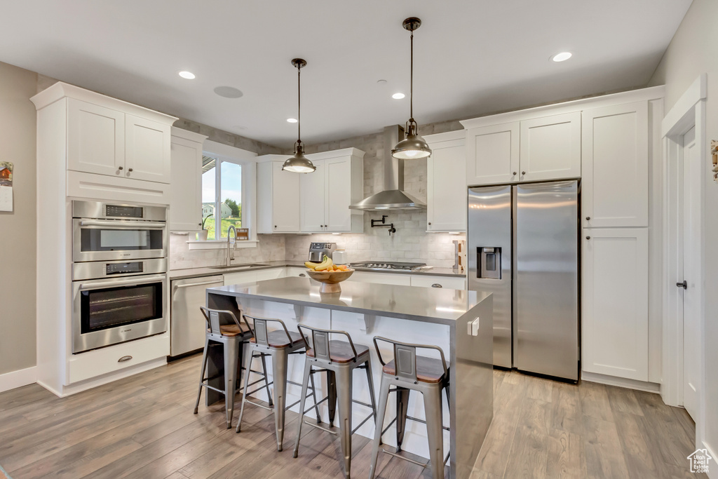 Kitchen with stainless steel appliances, a sink, wall chimney range hood, light wood-type flooring, and backsplash