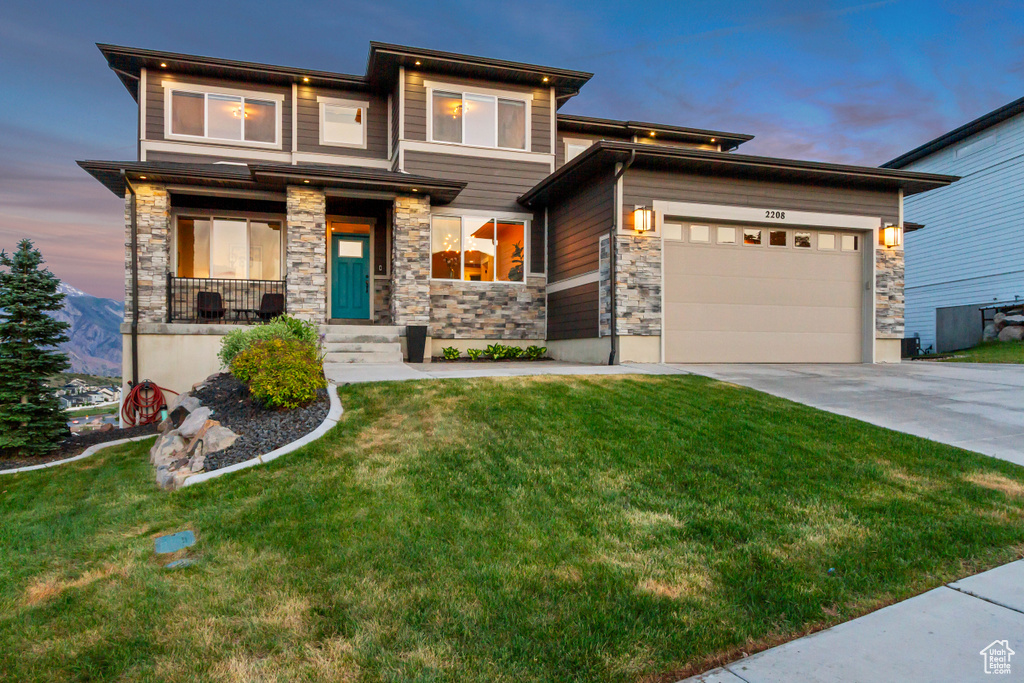 Prairie-style home featuring stone siding, concrete driveway, an attached garage, and a front yard