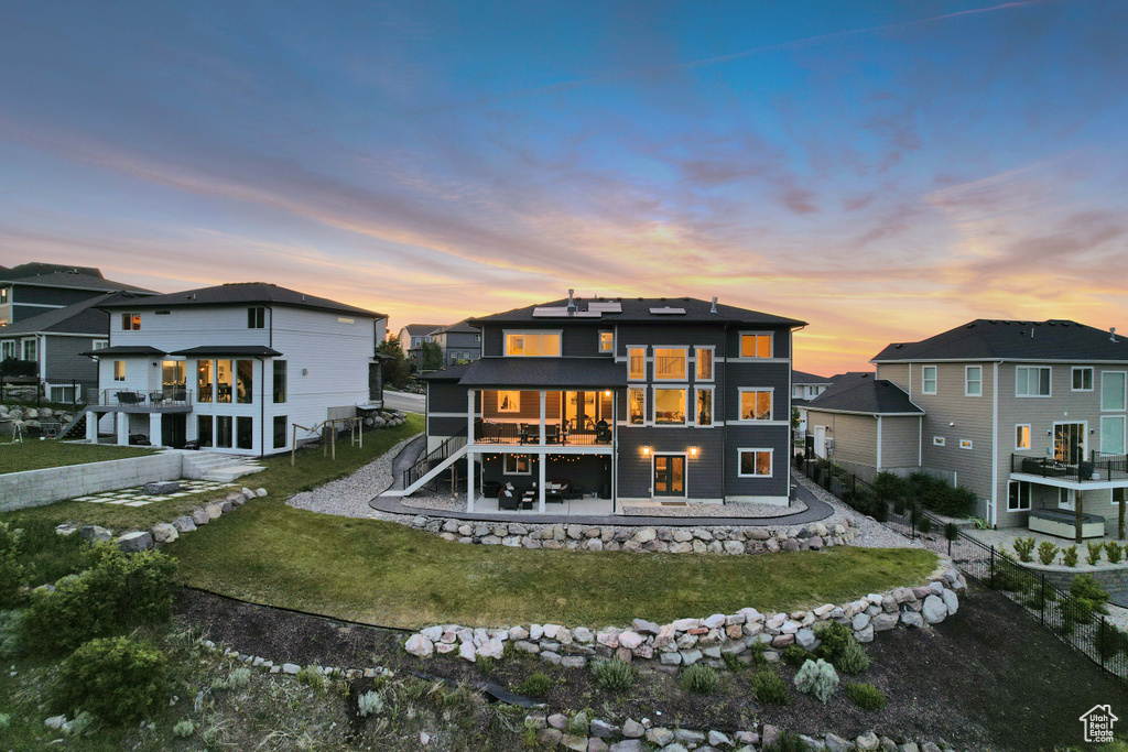 Back of house at dusk featuring a yard, stairs, a patio, and a residential view