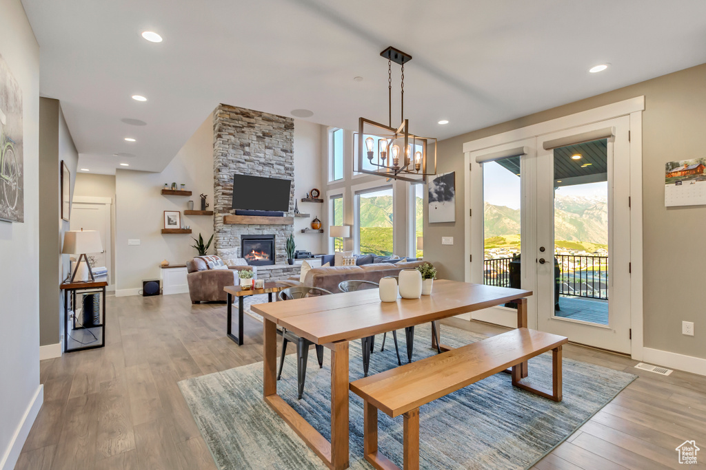 Dining area with a stone fireplace, french doors, light wood-style flooring, baseboards, and a chandelier