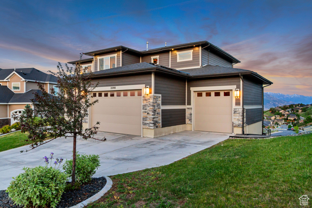Prairie-style house featuring driveway, a yard, stone siding, and an attached garage