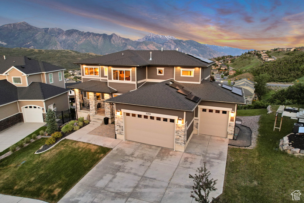 View of front facade with a mountain view, stone siding, a garage, concrete driveway, and a front yard
