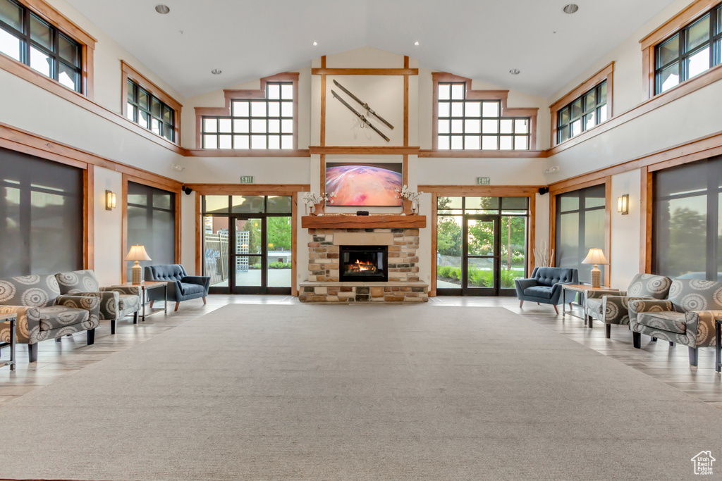 Living room featuring high vaulted ceiling, healthy amount of natural light, a stone fireplace, and carpet