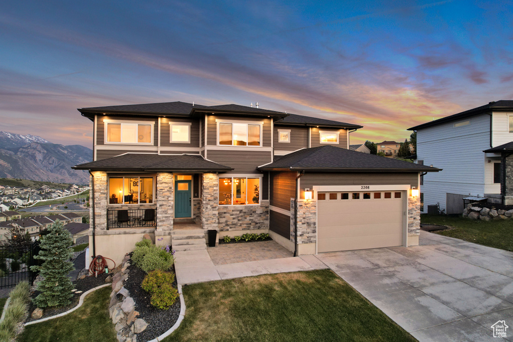 Prairie-style home featuring driveway, an attached garage, stone siding, covered porch, and a front yard