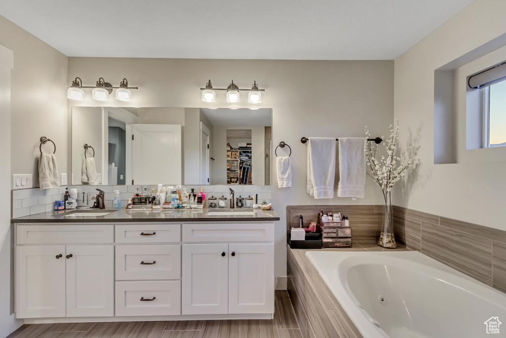 Full bathroom featuring double vanity, decorative backsplash, and a jetted tub