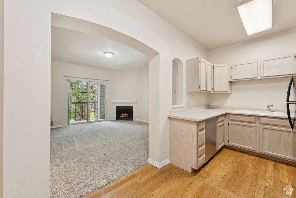 Kitchen featuring stainless steel dishwasher, a sink, light countertops, a fireplace, and baseboards