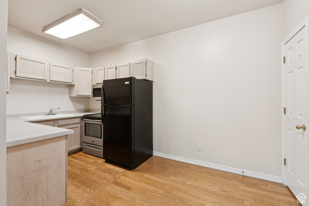 Kitchen with stainless steel appliances, light countertops, light wood finished floors, baseboards, and a sink