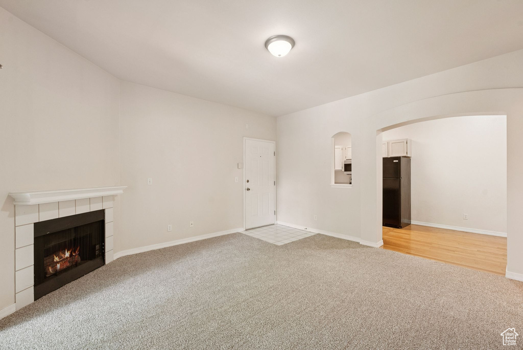 Unfurnished living room featuring light carpet, a fireplace, arched walkways, and baseboards