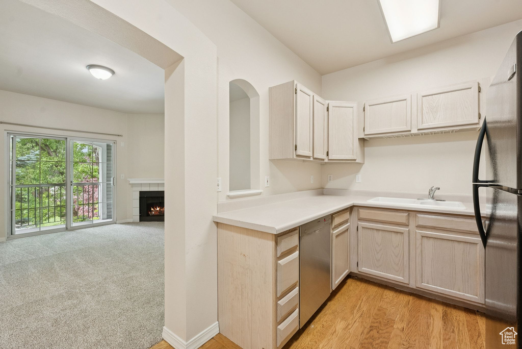 Kitchen featuring dishwasher, a sink, freestanding refrigerator, light countertops, and a tile fireplace