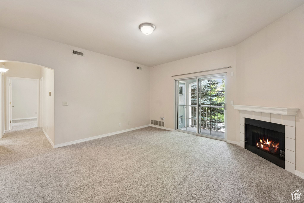 Unfurnished living room with light colored carpet, a fireplace, arched walkways, and baseboards