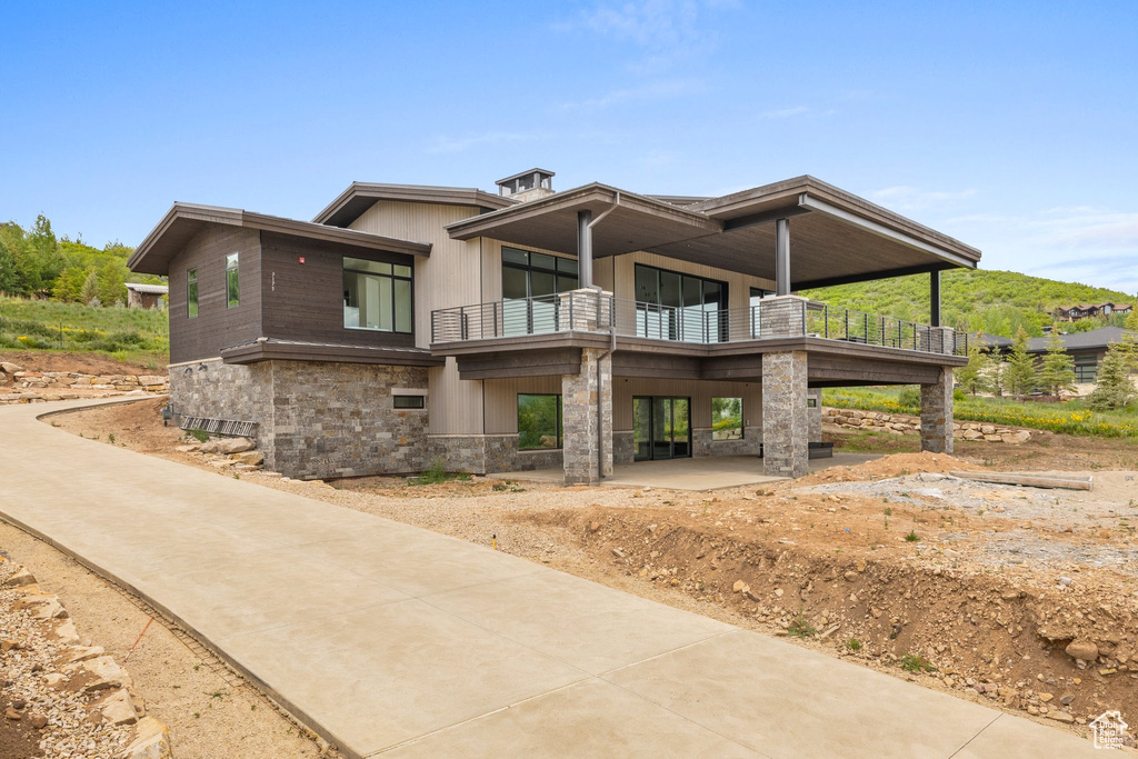 View of front facade with a balcony, stone siding, a patio area, and french doors
