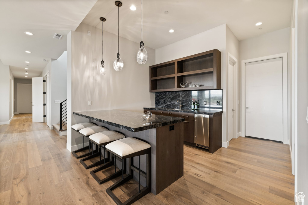 Kitchen featuring dark brown cabinets, a breakfast bar, open shelves, light wood finished floors, and recessed lighting