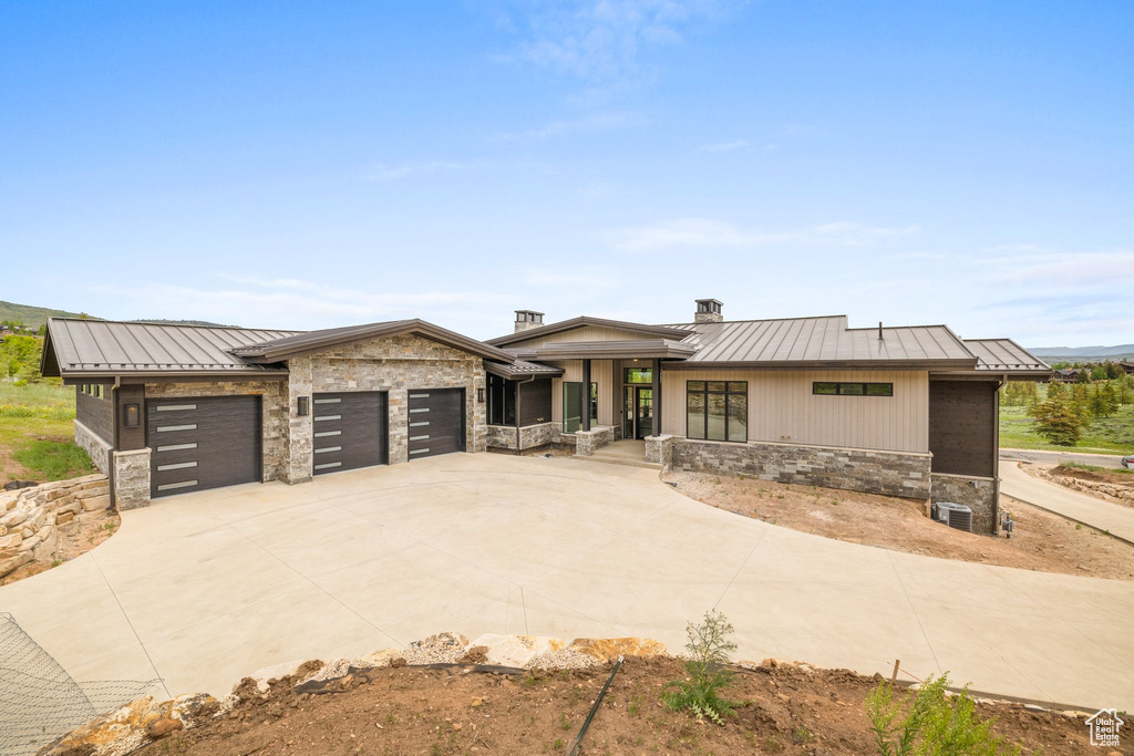 View of front of house featuring a standing seam roof, stone siding, a garage, and metal roof