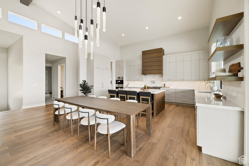 Kitchen with open shelves, a towering ceiling, modern cabinets, backsplash, and light wood finished floors