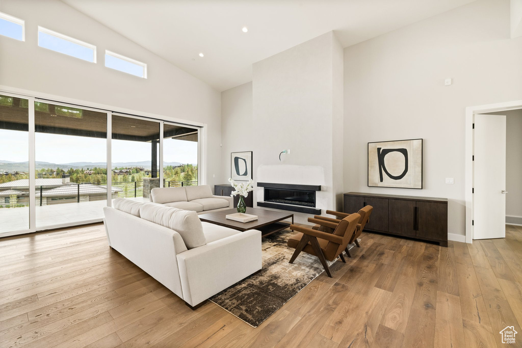 Living room with high vaulted ceiling, a glass covered fireplace, light wood-type flooring, baseboards, and recessed lighting