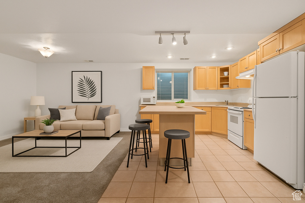 Kitchen featuring white appliances, light brown cabinets, under cabinet range hood, a breakfast bar area, and a kitchen island