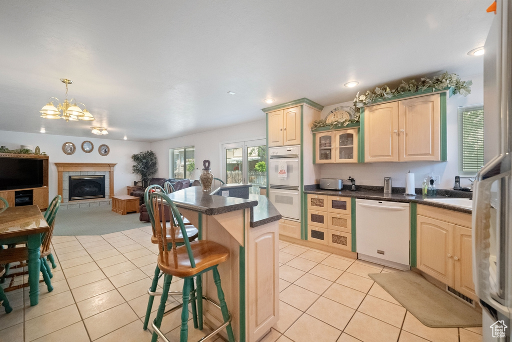 Kitchen featuring white appliances, light tile patterned floors, a chandelier, a breakfast bar, and dark countertops