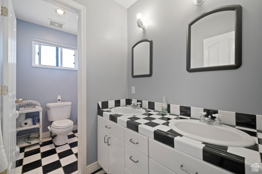 Bathroom with tile patterned floors, double vanity, toilet, and baseboards