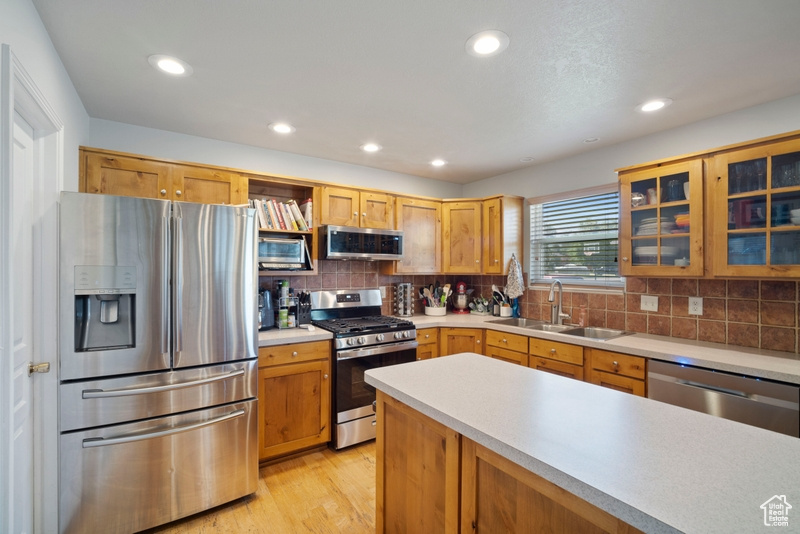 Kitchen featuring appliances with stainless steel finishes, a sink, light countertops, open shelves, and tasteful backsplash