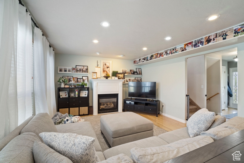 Living area featuring recessed lighting, a glass covered fireplace, light wood finished floors, baseboards, and stairway
