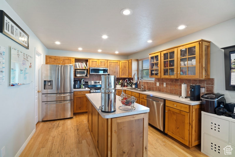 Kitchen with appliances with stainless steel finishes, a sink, decorative backsplash, a center island, and light countertops