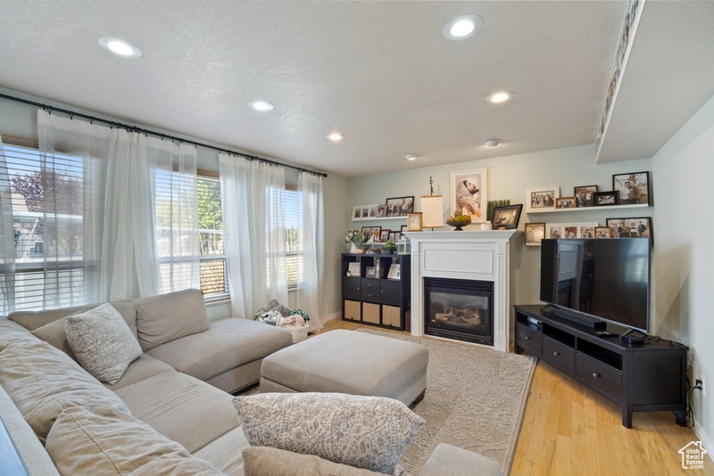 Living area featuring a glass covered fireplace, recessed lighting, light wood-style floors, and baseboards