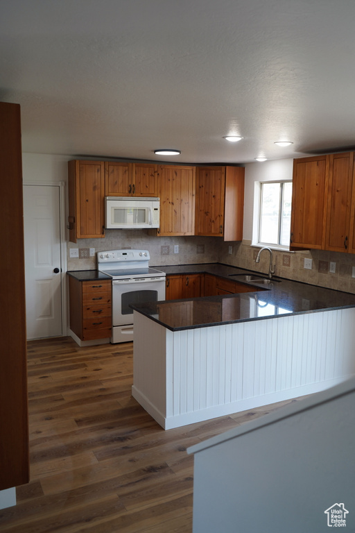 Kitchen with white appliances, a sink, dark wood finished floors, dark countertops, and tasteful backsplash