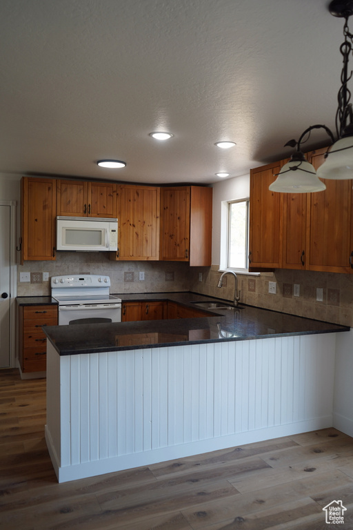 Kitchen featuring white appliances, a sink, brown cabinetry, dark countertops, and wood finished floors
