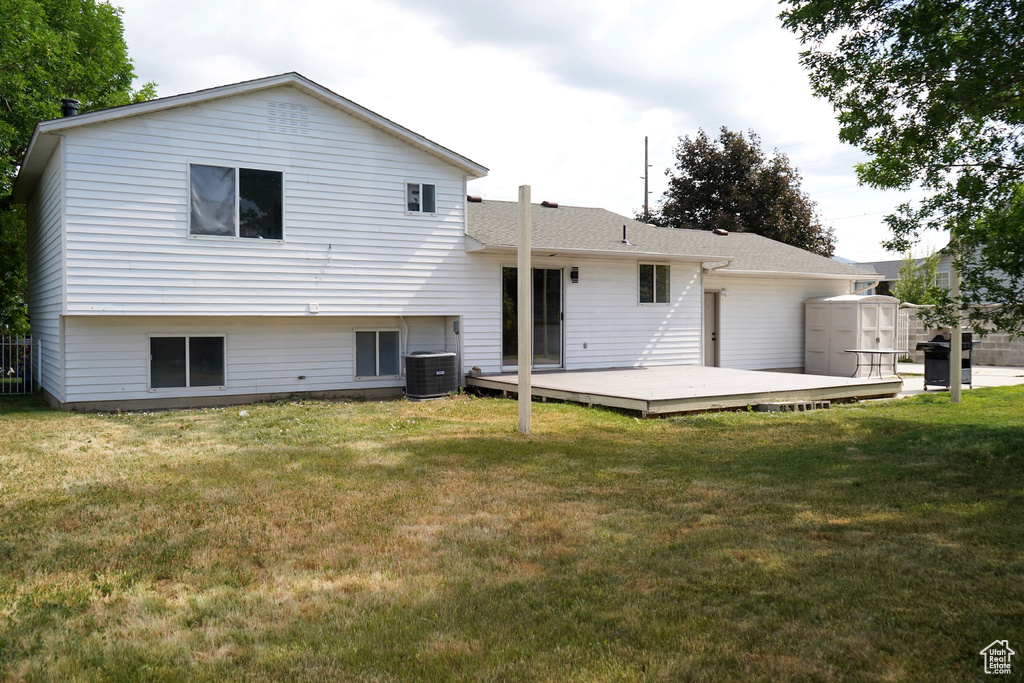 Rear view of property with a deck, a lawn, cooling unit, and roof with shingles