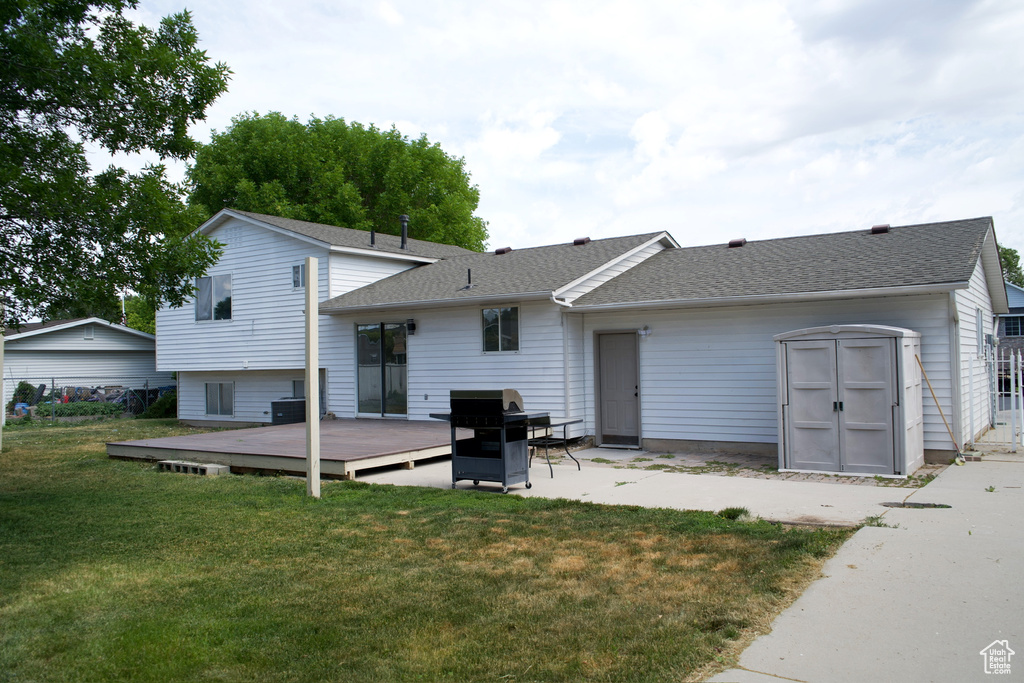 Rear view of property featuring a wooden deck, a yard, a shingled roof, and a patio