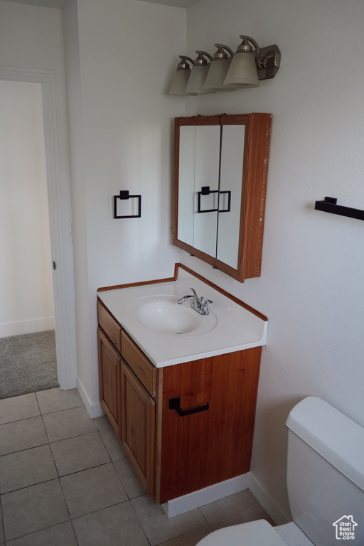 Half bathroom with toilet, vanity, baseboards, and tile patterned flooring