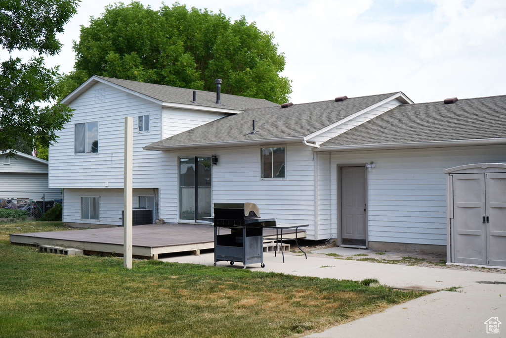 Rear view of house with a deck, roof with shingles, and a lawn
