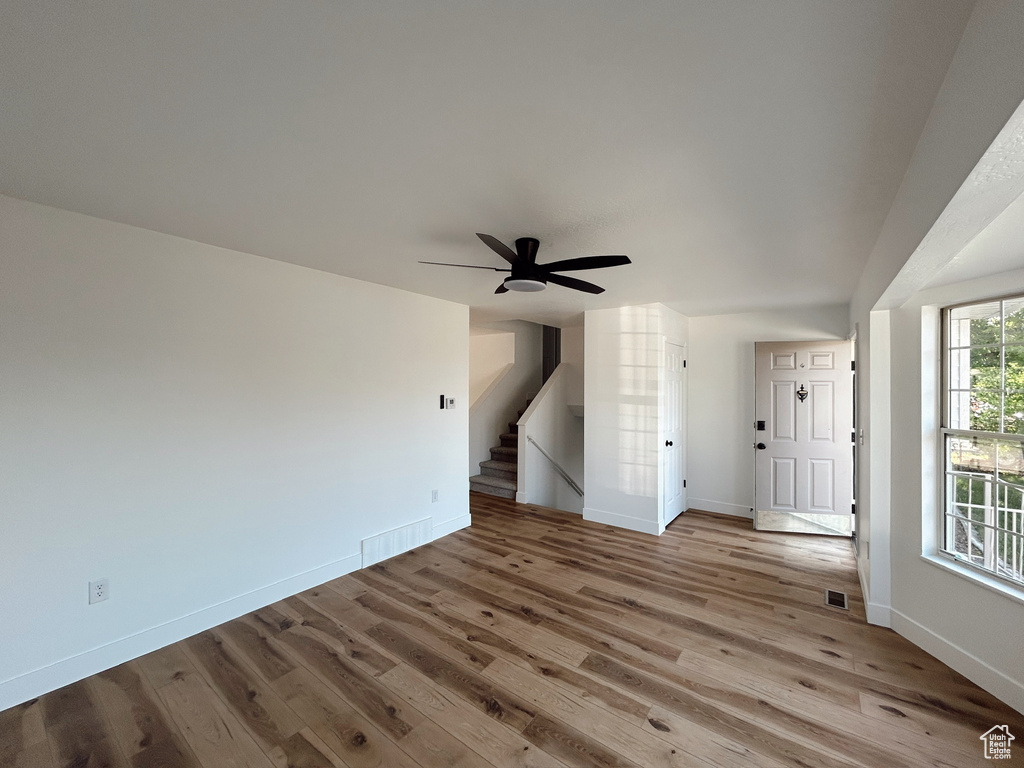 Unfurnished living room featuring wood finished floors, baseboards, ceiling fan, and stairs