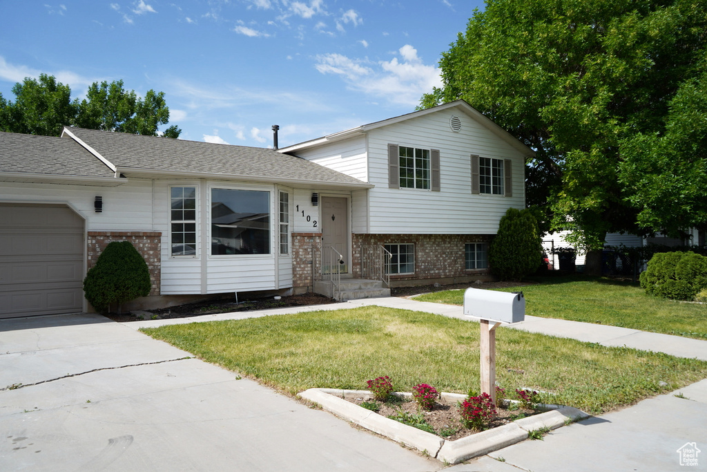 Tri-level home with brick siding, a garage, a front lawn, concrete driveway, and roof with shingles