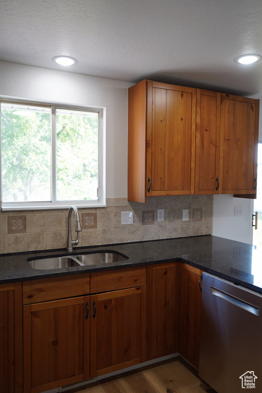 Kitchen with stainless steel dishwasher, a sink, brown cabinetry, and decorative backsplash