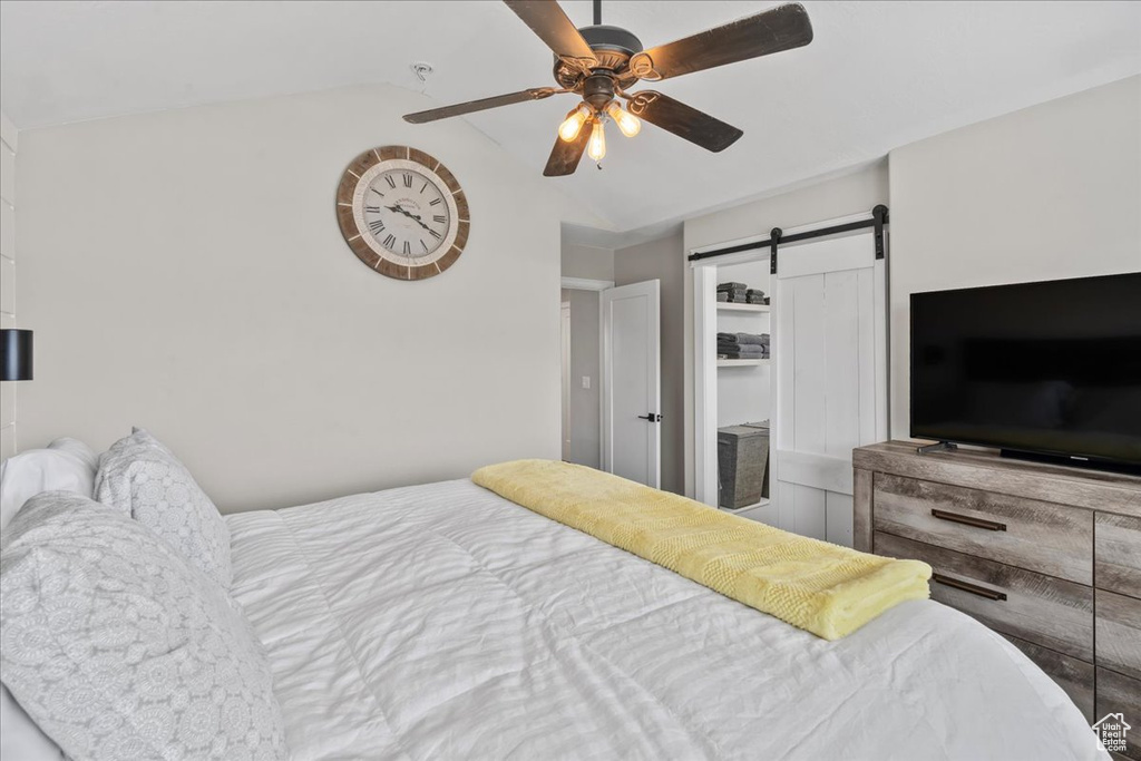 Bedroom with a barn door, vaulted ceiling, and ceiling fan