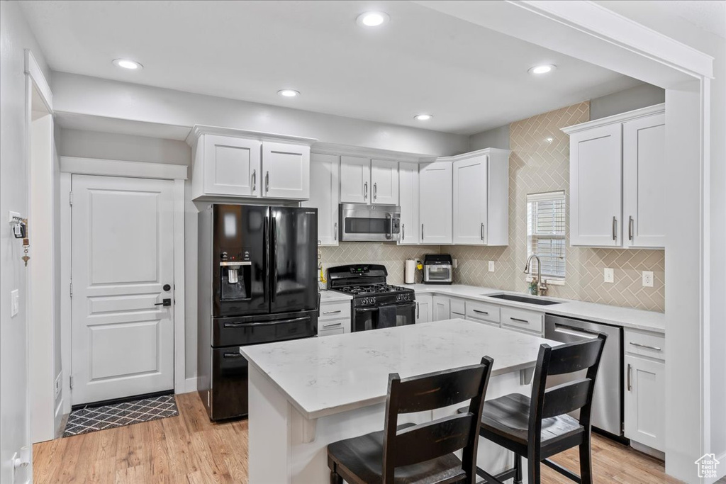 Kitchen featuring black appliances, a sink, white cabinets, a breakfast bar area, and light wood-type flooring