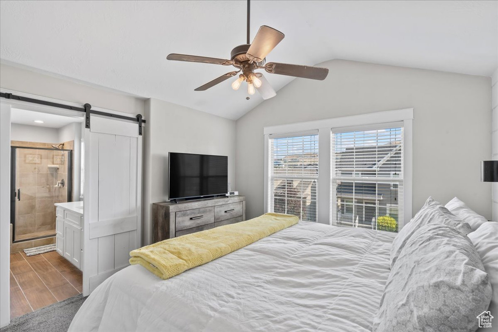 Bedroom with a barn door, wood finished floors, lofted ceiling, ceiling fan, and ensuite bath