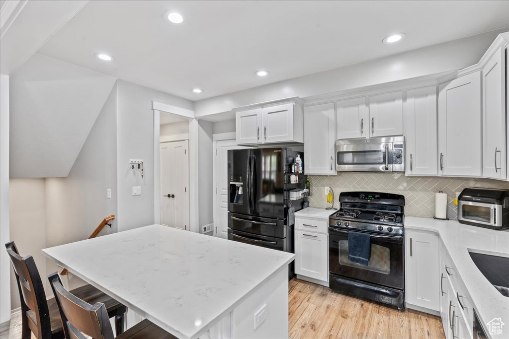 Kitchen with black appliances, white cabinetry, light wood finished floors, tasteful backsplash, and recessed lighting