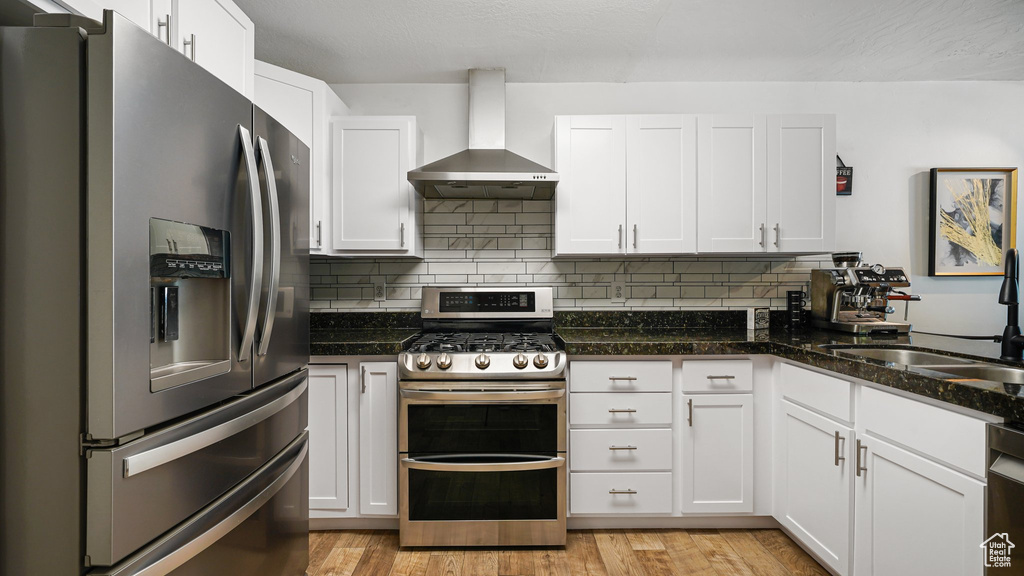 Kitchen featuring stainless steel appliances, wall chimney range hood, a sink, white cabinets, and backsplash