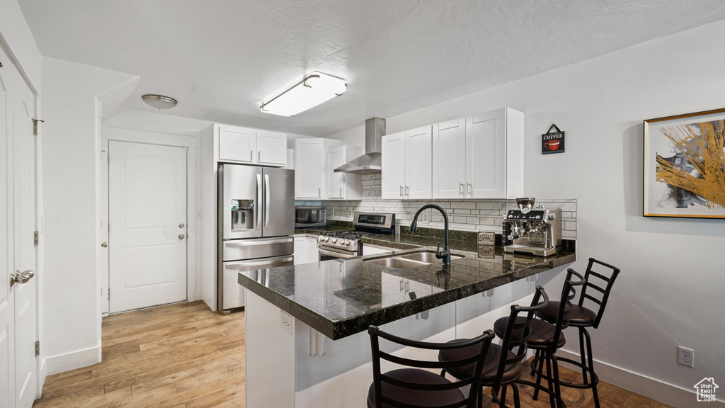Kitchen featuring stainless steel appliances, wall chimney exhaust hood, a sink, a peninsula, and decorative backsplash