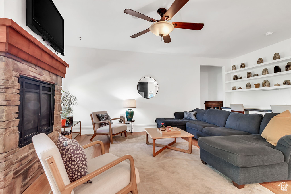 Living area featuring a stone fireplace, ceiling fan, built in shelves, and light wood-style flooring