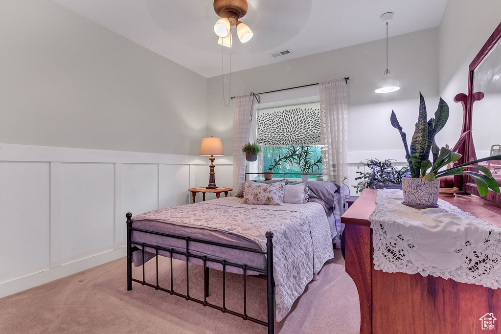 Carpeted bedroom with wainscoting, a decorative wall, and ceiling fan