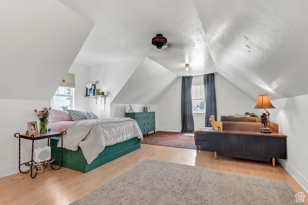 Bedroom with multiple windows, wood finished floors, vaulted ceiling, and baseboards