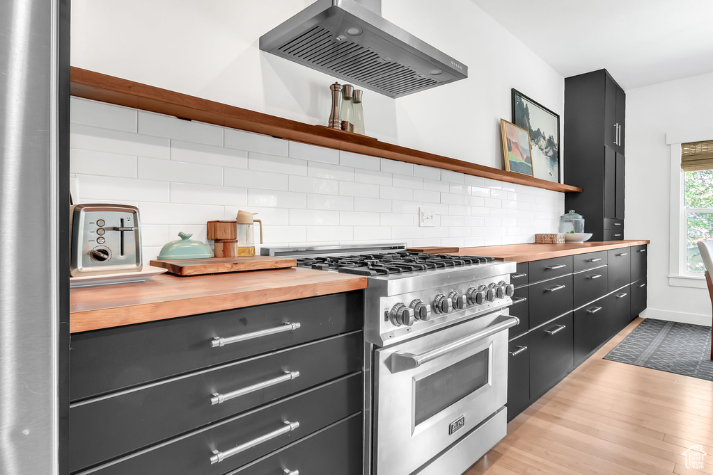 Kitchen with high end stove, extractor fan, open shelves, butcher block counters, and light wood-style floors